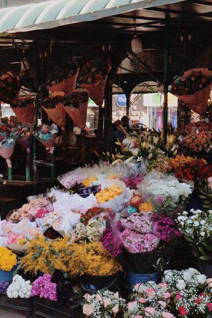 A vibrant outdoor flower market stall displaying an extensive array of fresh floral arrangements and bouquets. The arrangement includes roses, daisies, chrysanthemums, and various seasonal blooms in s
